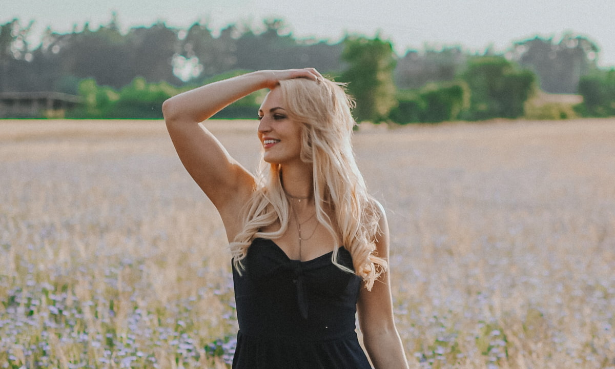 Pflegetipps Extensions Frau greift sich durch ihre langen blonden Haare in einem Blumenfeld