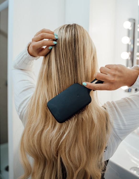 Extensions Tipps Haarpflege Frau kämmt sich ihre Extensions mit einer schwarzen Bürste