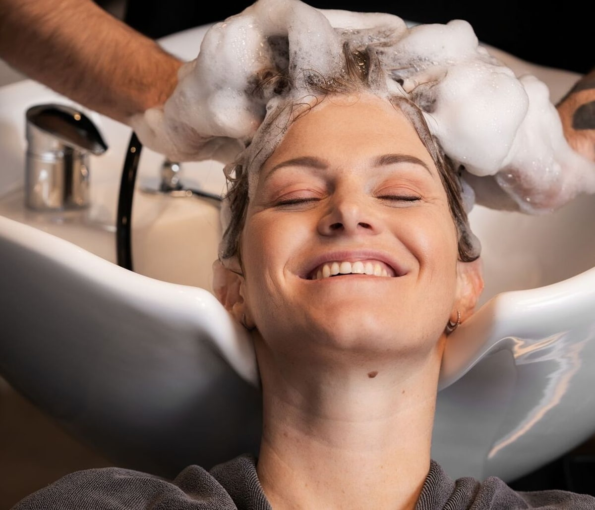 Tipps richtiges Haarewaschen Frau bekommt beim Friseur eine Haarwäsche und lächelt