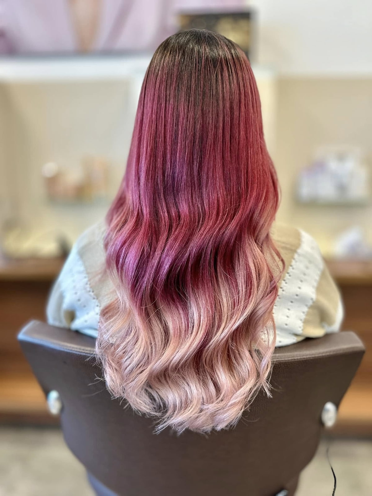 Dauerhaft strahlende Haarfarbe Frau sitzt in einem Friseurstuhl, man sieht ihre pink gefärbten Haare von hinten