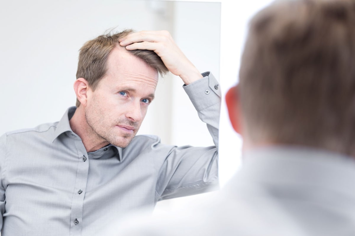 Haarprobleme Haarausfall Tipps Man blickt in den Spiegel und betrachtet seinen Haarverlust