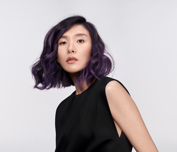 Asiatische Frau mit lila gefärbten Haaren blickt in die Kamera