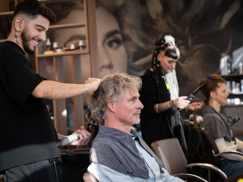 Stylist föhnt die Haare eines Kunden 
