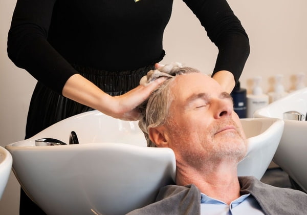 Haarpflege Männer Grundlagen Friseur Mitarbeiterin wäscht einem Mann mit grauen Haar die Haare im Salon
