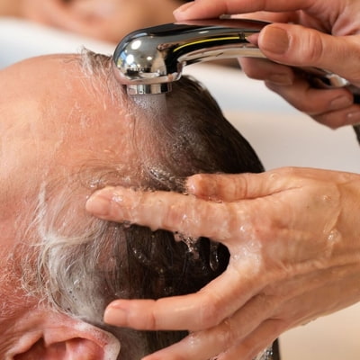 Pflegetipps Männerhaar Ein älterer Mann mit grauen Haaren bekommt eine Kopfmassage während des Waschvorgangs im Salon