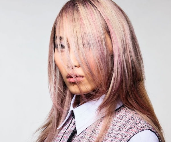Portrait einer Frau mit blonden Haaren und pinken Strähnen, deren Stirnfransen ihr Gesicht verdecken