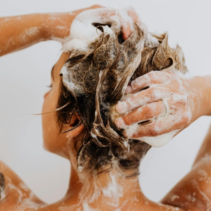 Eine Frau wäscht sich die Haare und hat viel Schaum in den Haaren